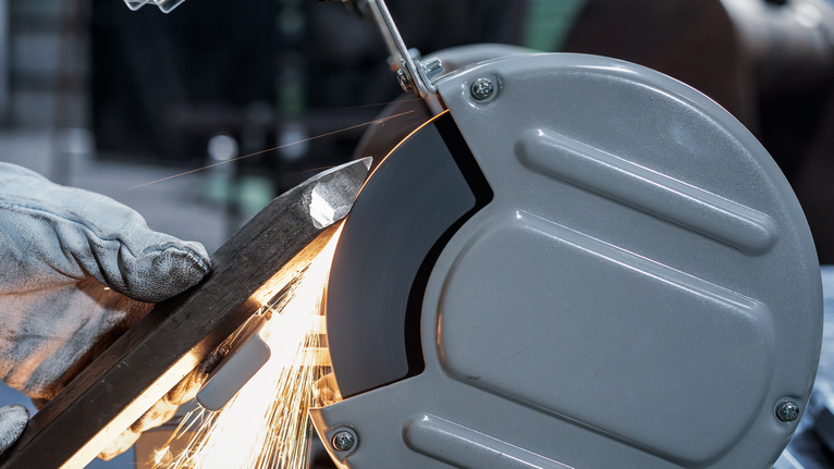 Một người mặc đồ bảo hộ đang mài một thanh kim loại bằng máy mài.