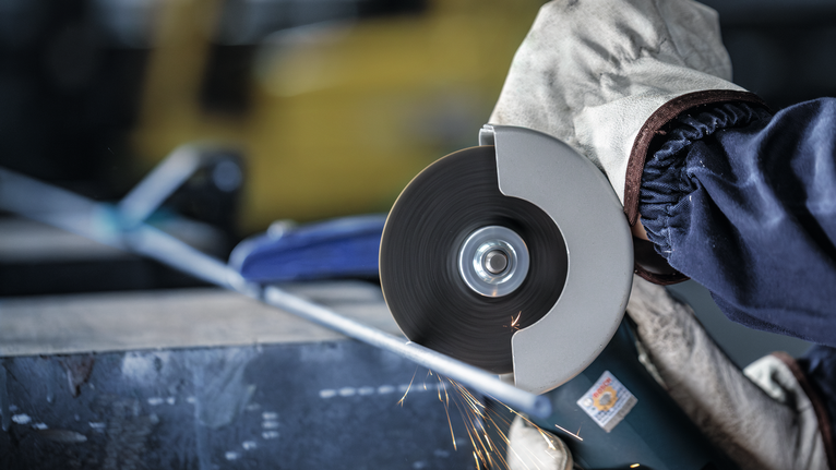 Người mặc đồ bảo hộ đang cắt ống kim loại bằng máy mài góc.