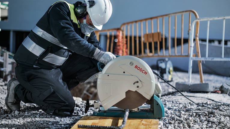 Một công nhân mặc đồ bảo hộ đang cắt thép cây bằng máy cưa tại một công trường xây dựng.