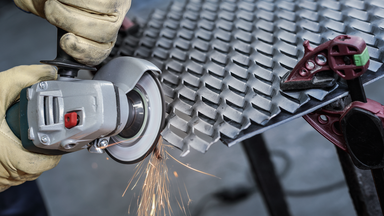 Người đeo thiết bị an toàn sử dụng máy mài góc để cắt tấm kim loại.