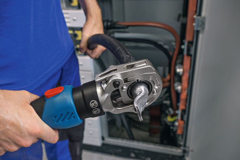 Một người sử dụng dụng cụ bấm thủy lực không dây trên một sợi cáp dày gần bảng điện.