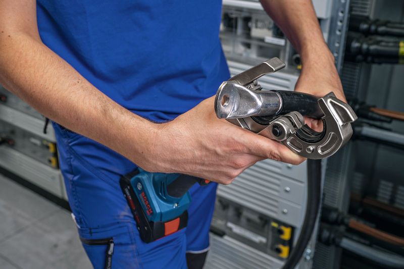 Một người mặc thiết bị an toàn đang sử dụng dụng cụ bấm thủy lực không dây trên cáp.