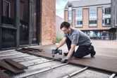 Một người mặc đồ bảo hộ đang lắp đặt ván sàn bằng máy khoan không dây.