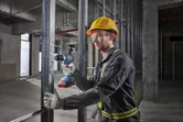 Một người mặc đồ bảo hộ đang khoan vào khung kim loại tại một công trường xây dựng.
