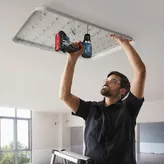 Một người mặc thiết bị an toàn đang sử dụng máy khoan điện để lắp đèn trần.