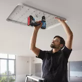 Một người mặc đồ bảo hộ đang sử dụng máy khoan không dây để lắp đèn trần.