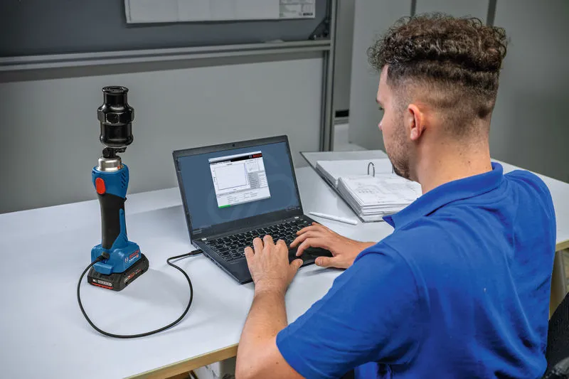 Một người đang kết nối một công cụ đục lỗ thủy lực không dây với máy tính xách tay trên bàn làm việc.