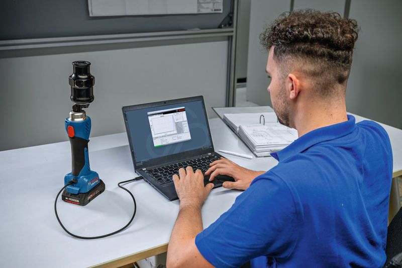 Một người đang kết nối một công cụ đục lỗ thủy lực không dây với máy tính xách tay trên bàn làm việc.