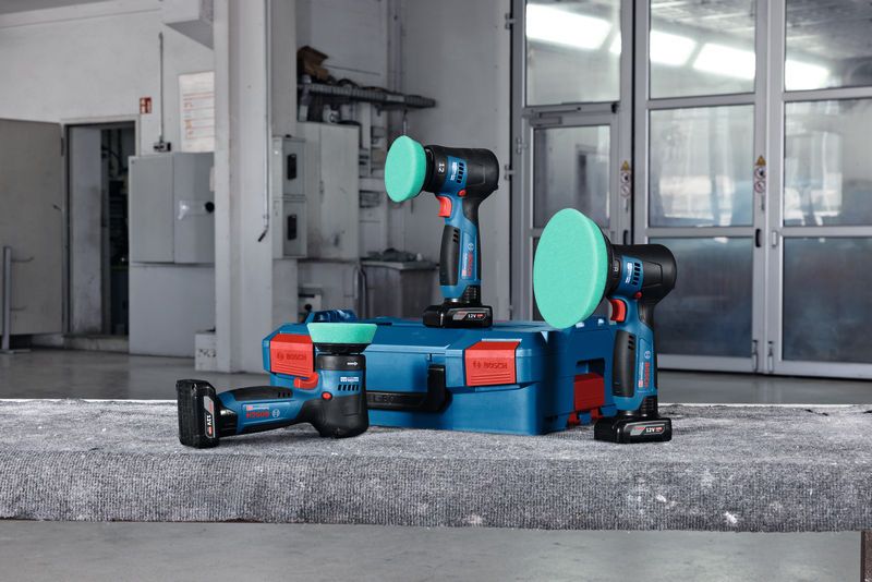 Ba máy đánh bóng không dây có miếng đệm màu xanh lá cây được đặt trên một chiếc hộp màu xanh trong một xưởng.