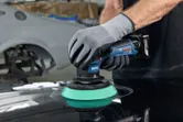 Một người mặc đồ bảo hộ đang đánh bóng bề mặt ô tô bằng máy đánh bóng không dây.
