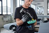 Một người mặc đồ bảo hộ đang đánh bóng máy đánh bóng không dây trong xưởng sửa chữa ô tô.