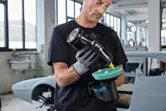 Một người mặc đồ bảo hộ đang đánh bóng máy đánh bóng không dây trong xưởng sửa chữa ô tô.