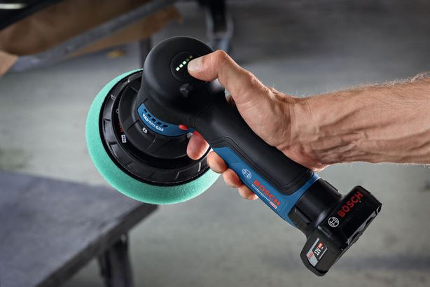 GPX 12V-125 Một người đang cầm máy đánh bóng không dây có miếng đệm xốp màu xanh lá cây gần bàn làm việc.