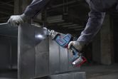 Một người mặc đồ bảo hộ đang cắt tấm kim loại bằng máy cưa lọng không dây.