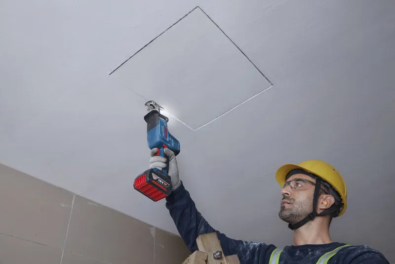 GSA 18V-24 Một người mặc đồ bảo hộ đang cắt tấm trần nhà bằng máy cưa lọng.