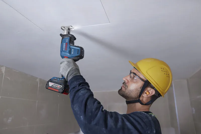GSA 18V-24 Một người mặc đồ bảo hộ đang sử dụng máy cưa lọng để cắt vào tấm trần nhà.