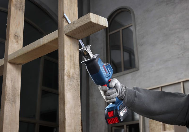 Một người mặc đồ bảo hộ đang sử dụng máy cưa lọng để cắt các thanh gỗ.