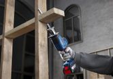 Một người mặc đồ bảo hộ đang sử dụng máy cưa lọng để cắt các thanh gỗ.