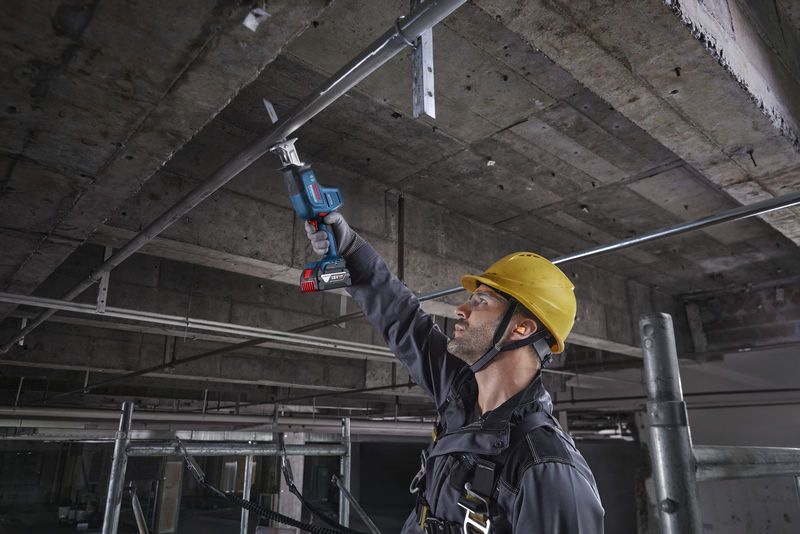 Một người mặc đồ bảo hộ sử dụng máy cưa lọng để cắt một ống kim loại ở phía trên.