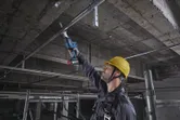 Một người mặc đồ bảo hộ sử dụng máy cưa lọng để cắt một ống kim loại ở phía trên.