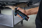 Một người đang cầm máy chà nhám quỹ đạo không dây gần bàn làm việc bằng kim loại.