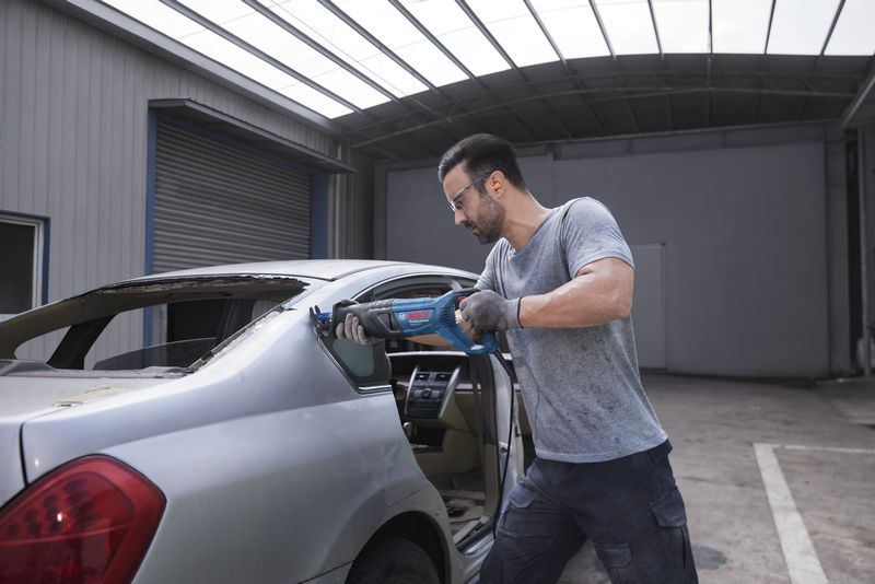 Người mặc thiết bị an toàn sử dụng cưa lọng để cắt khung cửa sổ sau của ô tô.