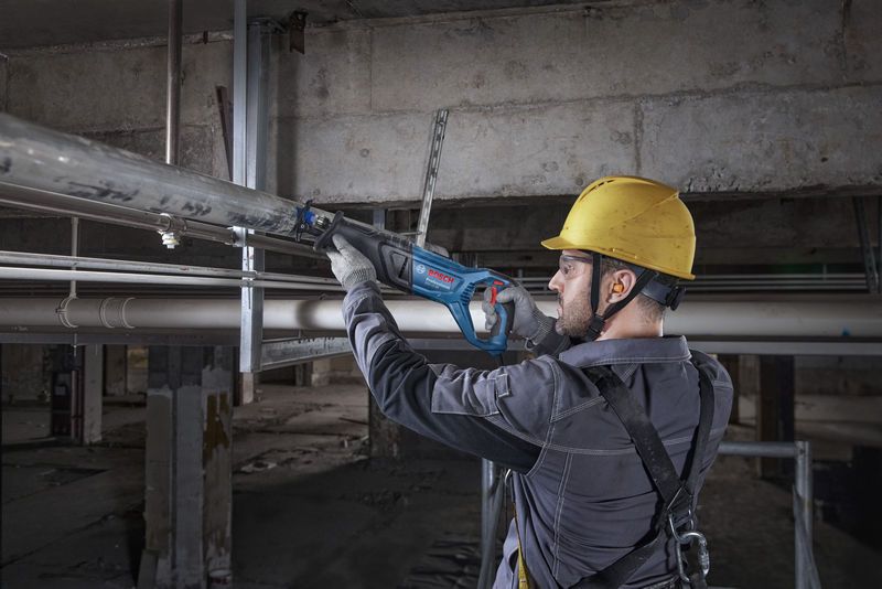 Một người mặc đồ bảo hộ đang cắt một ống kim loại bằng cưa lọng.