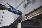 Một người mặc đồ bảo hộ đang vận hành máy cưa lọng để cắt một thanh gỗ.