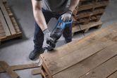 Một người mặc đồ bảo hộ đang sử dụng máy cưa lọng để cắt một tấm pallet gỗ.