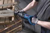 Một người mặc đồ bảo hộ đang sử dụng máy cưa lọng để cắt pallet gỗ.