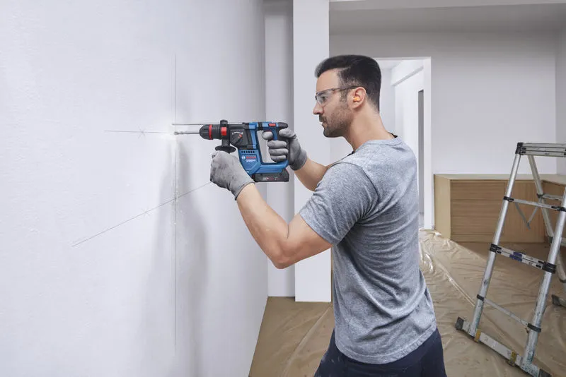 GBH 18V-18 X Một người mặc đồ bảo hộ sẽ khoan vào bức tường được đánh dấu bằng búa quay không dây.