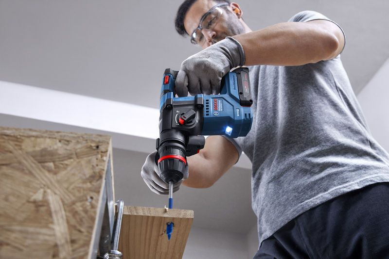 GBH 18V-18 X Một người mặc đồ bảo hộ đang khoan gỗ bằng búa quay không dây.