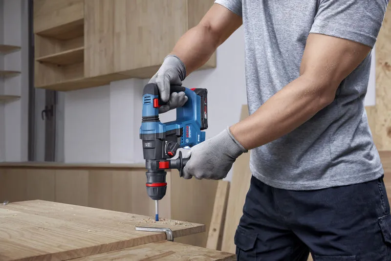 GBH 18V-18 X Một người mặc đồ bảo hộ đang khoan gỗ bằng búa quay không dây.