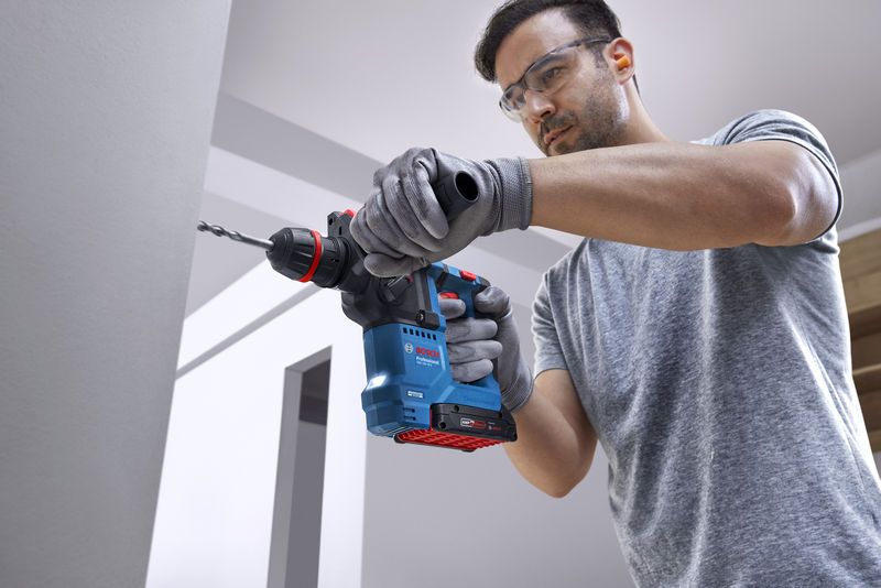 Một người mặc đồ bảo hộ đang khoan vào tường bê tông bằng máy khoan quay không dây.