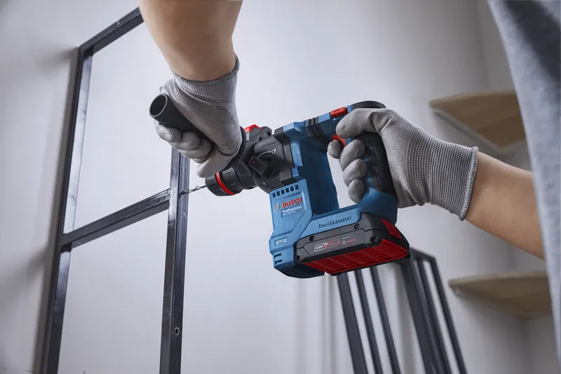 GBH 18V-18 X Một người mặc đồ bảo hộ đang khoan lỗ trên khung kim loại bằng búa quay không dây.