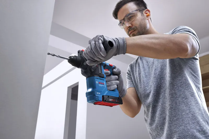 Người mặc đồ bảo hộ khoan tường bằng búa quay.