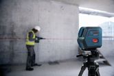 Một người mặc thiết bị an toàn sử dụng máy khoan trong khi máy cân bằng laser chiếu một đường màu đỏ.