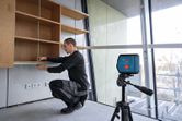 Một người đang căn chỉnh kệ bằng máy cân bằng laser trong một căn phòng hiện đại.