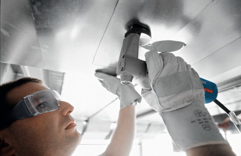 Một người mặc đồ bảo hộ sử dụng kéo để cắt một tấm kim loại.