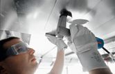 Một người mặc đồ bảo hộ đang dùng kéo điện cắt tấm kim loại trên cao.