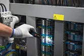 Một người mặc thiết bị an toàn đang kiểm tra hệ thống dây điện trong bảng điều khiển bằng máy kiểm tra điện áp.