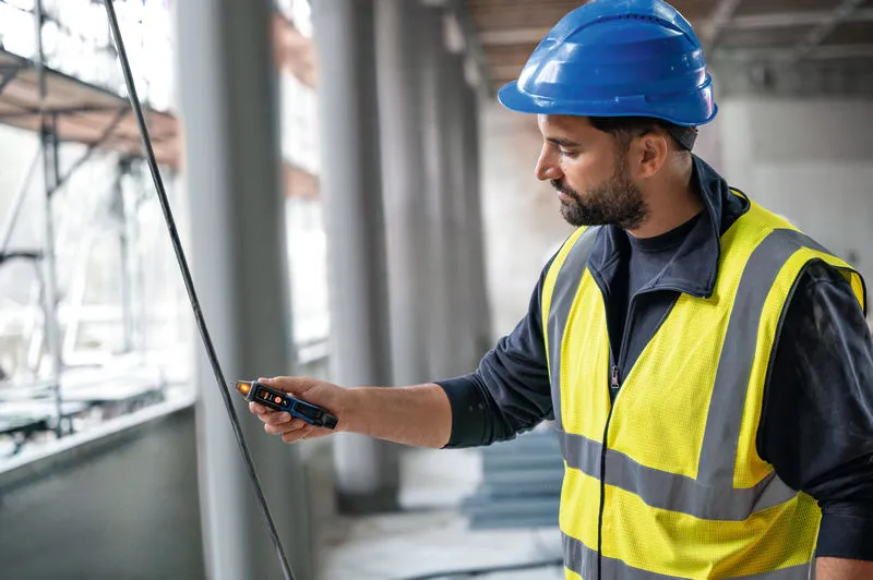 Một người mặc thiết bị an toàn đang kiểm tra cáp bằng máy kiểm tra điện áp không tiếp xúc.