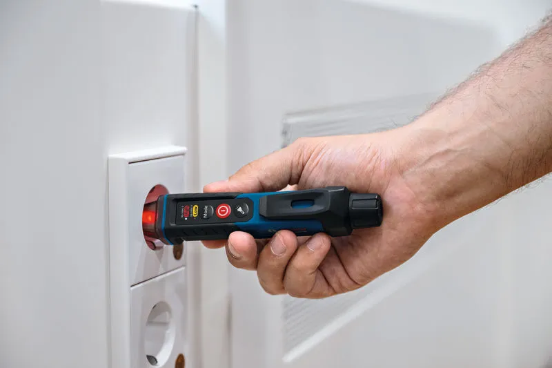 Một người sử dụng máy kiểm tra điện áp không tiếp xúc gần ổ cắm điện.