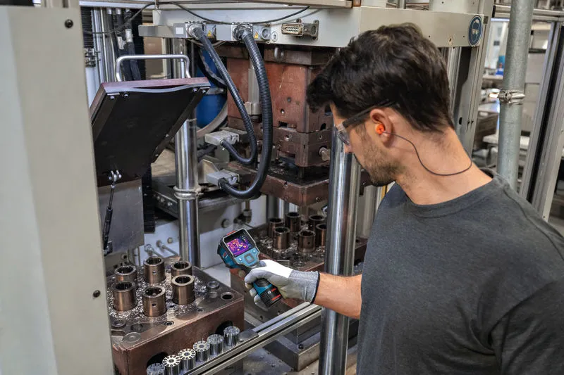 Một người mặc đồ bảo hộ đang kiểm tra máy móc công nghiệp bằng camera nhiệt.