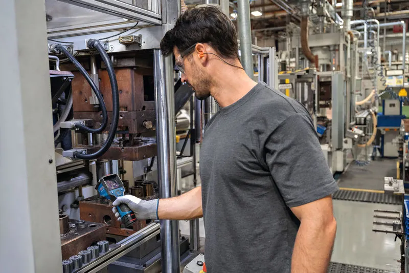 Một người mặc đồ bảo hộ đang kiểm tra máy móc bằng camera nhiệt trong một nhà máy.