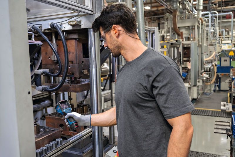 Một người mặc đồ bảo hộ đang kiểm tra máy móc bằng camera nhiệt trong một nhà máy.