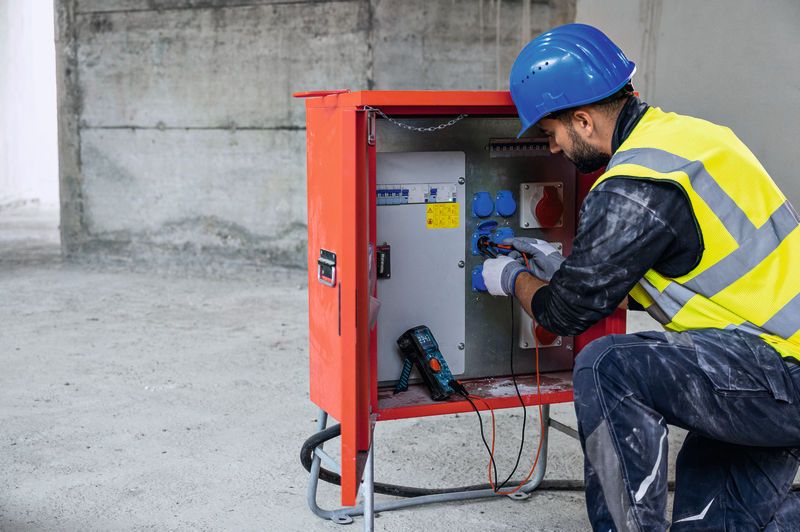 Một người mặc thiết bị an toàn sử dụng đồng hồ vạn năng kỹ thuật số để kiểm tra bảng điện.