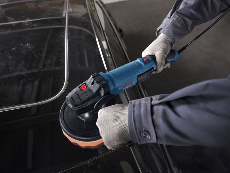 Một người mặc đồ bảo hộ đang đánh bóng nóc xe bằng máy đánh bóng điện.