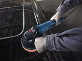 Một người mặc đồ bảo hộ đang đánh bóng nóc xe bằng máy đánh bóng điện.