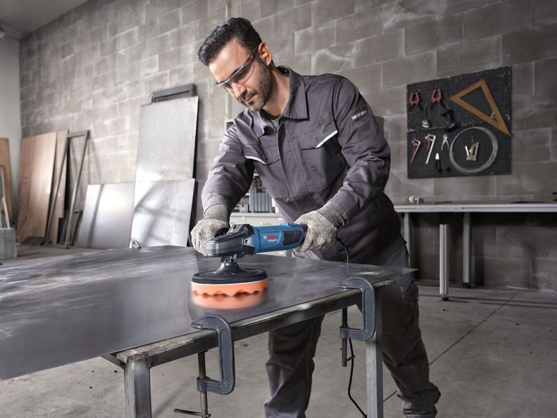 Một người mặc đồ bảo hộ đang đánh bóng tấm kim loại bằng dụng cụ điện.